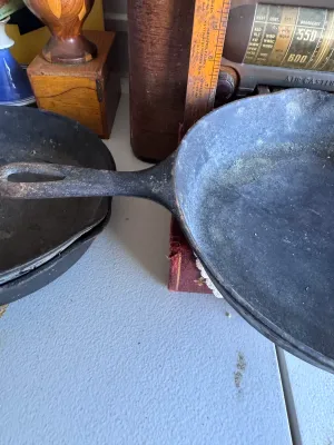Sale Photo Thumbnail #270: A vintage Griswold No. 7 cast iron skillet, marked with the classic Griswold logo, 'ERIE PA., U.S.A.', and model number '701 E'. Features dual pour spouts and a teardrop handle. The skillet shows signs of age and use, including surface buildup, minor rust