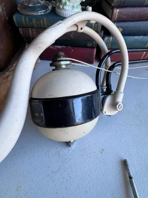Sale Photo Thumbnail #123: A vintage medical/dental equipment component, manufactured by Ritter. Features a spherical cream and black enameled metal housing suspended on a curved tubular arm with pulley cords. Shows typical wear, scuffs, and paint loss consistent with age and use. 