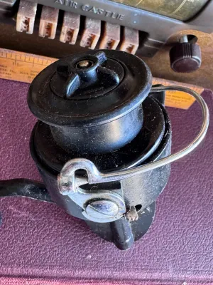 Sale Photo Thumbnail #283: A vintage Mitchell spinning fishing reel featuring a classic black finish. The body is marked with 'Made in France'. It shows some signs of wear and age-appropriate use, including light surface dust and minor scuffs, but remains in solid cosmetic conditio