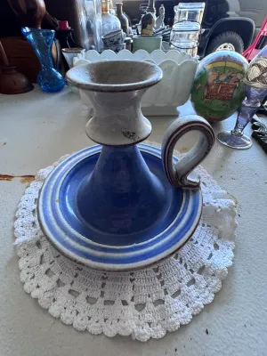 Sale Photo Thumbnail #335: A charming vintage ceramic chamberstick style candlestick holder featuring a finger loop handle. Decorated in a glazed blue and off-white color scheme with brown trim accents. Shows some light wear and minor glaze imperfections consistent with age and use