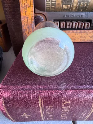 Sale Photo Thumbnail #300: A vintage small glass bud vase featuring a flared clear glass top section accented with gold-toned horizontal bands and a gold-gilded rim. The bulbous base is made of frosted light green glass, hand-painted with a delicate white flower and green leaves. M