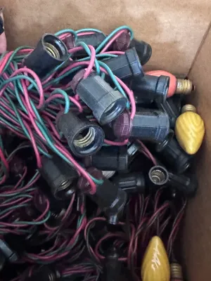 Sale Photo Thumbnail #112: A large estate collection of vintage Christmas lighting. Includes multiple green and red/pink insulated wire light strings with black sockets, a vintage red cardboard box of 'Twinkling Lamps' by World Wide, and a large assortment of loose ceramic and pain