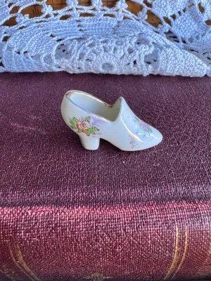 Sale Photo Thumbnail #237: A vintage miniature porcelain shoe figurine featuring delicate hand-painted floral details and gold-gilded trim. The bottom is stamped in red with 'MADE IN OCCUPIED JAPAN', dating this piece to the post-WWII occupation period (1945–1952). It is in good 