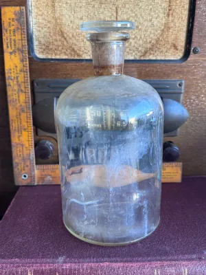 Sale Photo Thumbnail #342: An antique or vintage clear glass apothecary/chemical bottle featuring its original ground glass stopper. The bottom is embossed with 'T.C.W. CO. U.S.A.', indicating it was manufactured by the T.C. Wheaton Glass Company in Millville, New Jersey, USA. The 