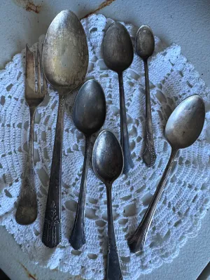 Sale Photo Thumbnail #279: An assortment of 7 vintage silverplated flatware pieces, including five spoons of various sizes, one serving spoon, and one pickle/cold meat fork. The pieces feature various ornate floral and classic handle patterns. Notable markings visible on the backs 