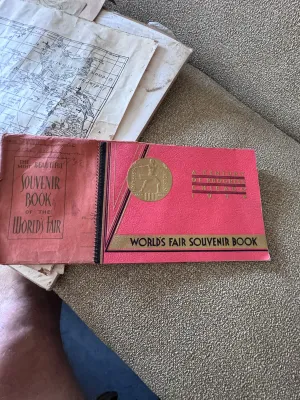 Sale Photo Thumbnail #157: An authentic 1934 souvenir book from the Chicago World's Fair, titled 'A Century of Progress'. This spiral-bound booklet features a textured pink cover with gold-embossed lettering and a central gold seal. Inside, it contains black-and-white photographic 
