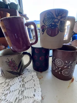Sale Photo Thumbnail #324: An eclectic collection of six vintage ceramic and stoneware mugs featuring distinct mid-century and retro designs. The set includes a brown mug marked 'W. Germany 926' on the bottom with stylized white floral/geometric patterns, a black mug with red spira