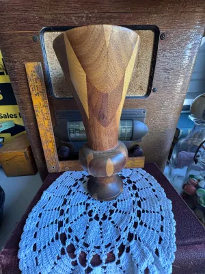 Sale Photo Thumbnail #257: A beautiful vintage hand-turned wooden vase featuring a segmented, inlaid geometric design with contrasting light and dark wood tones. The vase has a flared trumpet top and a bulbous pedestal base. The underside features a green felt ring and is stamped w