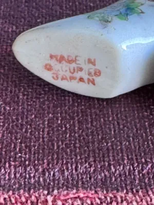 Sale Photo Thumbnail #239: A vintage miniature porcelain shoe figurine featuring delicate hand-painted floral details and gold-gilded trim. The bottom is stamped in red with 'MADE IN OCCUPIED JAPAN', dating this piece to the post-WWII occupation period (1945–1952). It is in good 