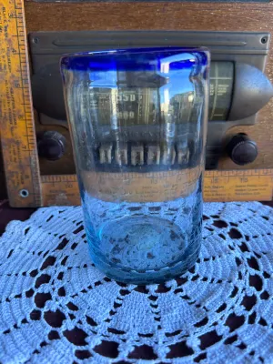 Sale Photo Thumbnail #248: A classic hand-blown drinking glass featuring a vibrant cobalt blue rim and a subtle light blue tint to the body. This rustic tumbler shows characteristic artisanal details, including small trapped air bubbles (seed bubbles) and a rough pontil scar on the