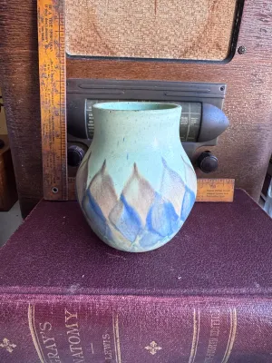 Sale Photo Thumbnail #50: A vintage art pottery vase from Weller Pottery, featuring a matte glaze with a stylized flame or leaf pattern in shades of blue, tan, and light green. Made in the USA. Measures approximately 6 inches tall. The underside shows hand-incised markings. Condit