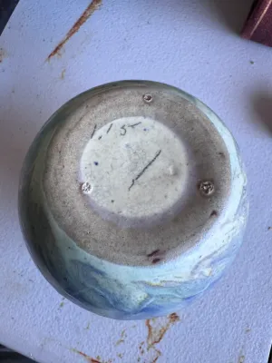 Sale Photo Thumbnail #52: A vintage art pottery vase from Weller Pottery, featuring a matte glaze with a stylized flame or leaf pattern in shades of blue, tan, and light green. Made in the USA. Measures approximately 6 inches tall. The underside shows hand-incised markings. Condit