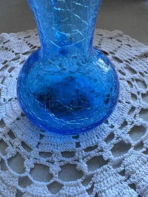 Sale Photo Thumbnail #333: A beautiful mid-century style hand-blown crackle glass pitcher or vase in a vibrant blue hue. Features a classic flared rim, a bulbous base, and an applied smooth glass handle. The piece shows characteristic crackle texture throughout the body. No maker's