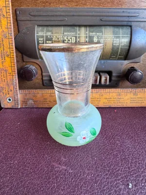 Sale Photo Thumbnail #298: A vintage small glass bud vase featuring a flared clear glass top section accented with gold-toned horizontal bands and a gold-gilded rim. The bulbous base is made of frosted light green glass, hand-painted with a delicate white flower and green leaves. M