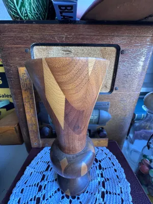 Sale Photo Thumbnail #260: A beautiful vintage hand-turned wooden vase featuring a segmented, inlaid geometric design with contrasting light and dark wood tones. The vase has a flared trumpet top and a bulbous pedestal base. The underside features a green felt ring and is stamped w