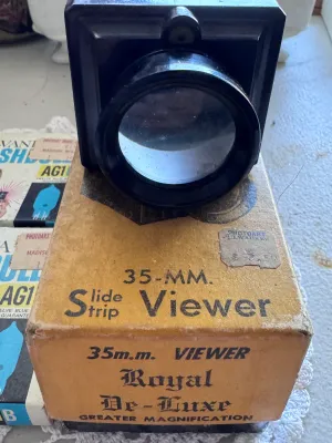 Sale Photo Thumbnail #311: Vintage photography lot featuring a Zarux 35mm Slide Strip Viewer (Royal De-Luxe model) made of dark bakelite/plastic, complete with its original cardboard box. The viewer is marked 'Zarux U.S.A.' on the bottom. Also included are two vintage boxes of Sylv