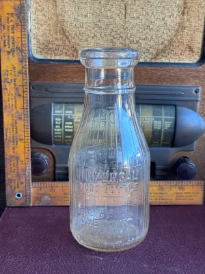 Sale Photo Thumbnail #304: A vintage clear glass one-pint milk bottle featuring embossed lettering. One side reads 'Universal Store Bottle / Sealed 1-11-14 / One Pint Liquid / Reg. U.S. Pat. Off.' and features vertical ribbing. The reverse side is embossed with 'Store Bottle' and a