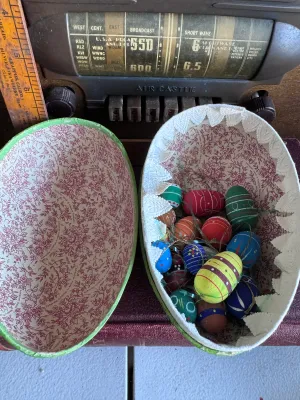 Sale Photo Thumbnail #193: A vintage large papier-mâché Easter egg candy container featuring a colorful illustration of bunnies in a hot air balloon on one side and a countryside landscape on the other. The interior is lined with a red floral pattern and features a white lace-sty