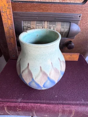 Sale Photo Thumbnail #51: A vintage art pottery vase from Weller Pottery, featuring a matte glaze with a stylized flame or leaf pattern in shades of blue, tan, and light green. Made in the USA. Measures approximately 6 inches tall. The underside shows hand-incised markings. Condit