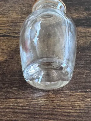 Sale Photo Thumbnail #235: A vintage miniature clear glass bottle, likely used for perfume, apothecary, or vanity display. Features a bulbous body shape with a cork stopper that includes a small glass ring top and amber-colored washer details. The glass shows some light age-related