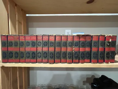 Sale Photo Thumbnail #8: Antique multi-volume set of Charles Dickens works, featuring red and black spines with ornate gold gilt detailing, showing some wear and tear on the edges.