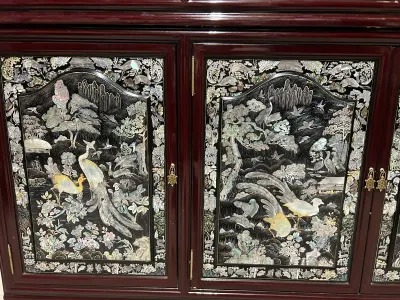Sale Photo Thumbnail #3: Vintage Asian-style lacquered wood cabinet featuring intricate mother-of-pearl inlay panels depicting peacocks, cranes, and deer in a lush landscape, accented with brass turtle-shaped door pulls.