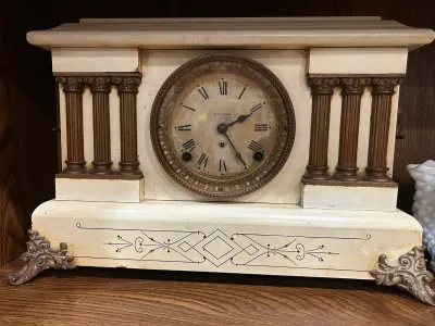 Sale Photo Thumbnail #9: Antique Seth Thomas mantel clock featuring an off-white painted wooden case with classical columns, ornate metal feet, and a distressed dial with Roman numerals.