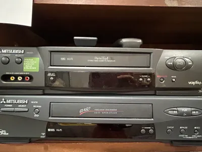 Sale Photo Thumbnail #13: Two Mitsubishi VHS players stacked on a wooden shelf, featuring a Mitsubishi HS-U530 VHS Hi-Fi Perfectape model on top and a Mitsubishi HS-U776 S-VHS Hi-Fi model below.