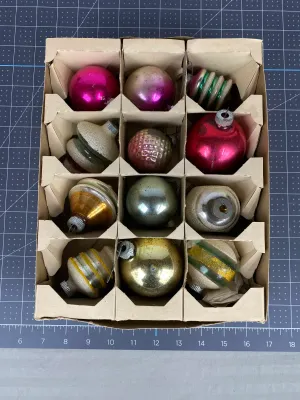 Collection of vintage glass Christmas ornaments in a cardboard organizer box, featuring various shapes, colors, and glitter details from...