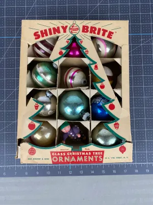 Vintage Shiny Brite glass Christmas tree ornaments in their original cardboard box, featuring a variety of colorful striped, solid, and...