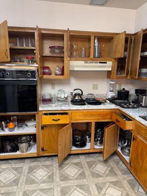 Sale Photo Thumbnail #15: Assorted kitchenware, small appliances, and cookware displayed on countertops and inside open wooden cabinets.