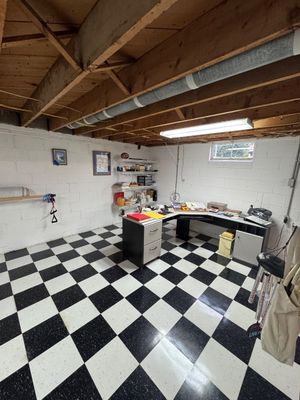 Sale Photo Thumbnail #35: Corner office desk with a black and white finish, paired with wall-mounted shelving and various office supplies in a basement room featuring black and white checkered flooring.