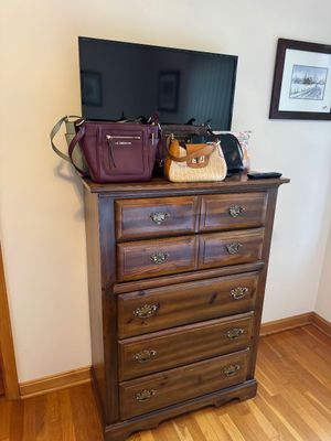 Sale Photo Thumbnail #20: Rustic pine tallboy dresser with brass batwing pulls, displaying a selection of women's handbags and a flat-screen television.