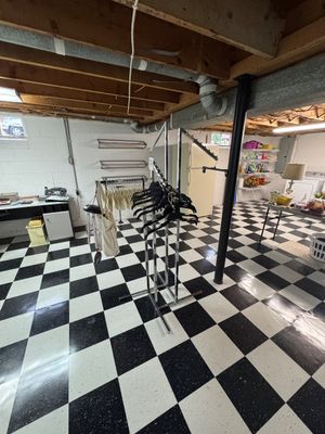 Sale Photo Thumbnail #33: Chrome retail clothing racks with black hangers, set in a basement with black and white checkered flooring.