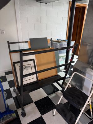 Sale Photo Thumbnail #37: Black metal rolling art storage rack holding framed artwork and mat boards, shown alongside a Cosco two-step folding step stool.