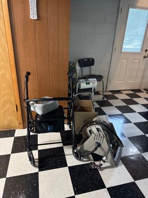 Sale Photo Thumbnail #36: Black four-wheeled rolling walker with a padded seat and under-seat storage bag, shown alongside a plastic garden hose reel on a black and white checkered floor.
