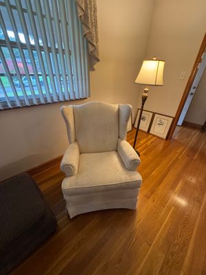 Sale Photo Thumbnail #9: Traditional wingback armchair upholstered in a cream-colored damask fabric, paired with a classic brass floor lamp and framed botanical prints.