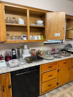 Sale Photo Thumbnail #18: Assorted kitchenware and small appliances, including a Cuisinart ice cream maker, baking dishes, and glassware, displayed on a laminate countertop and inside wooden cabinets.