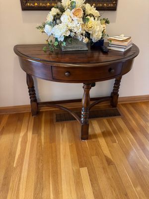 Sale Photo Thumbnail #3: Traditional dark wood demilune console table featuring a single drawer with round pulls, turned legs, and a curved stretcher base.