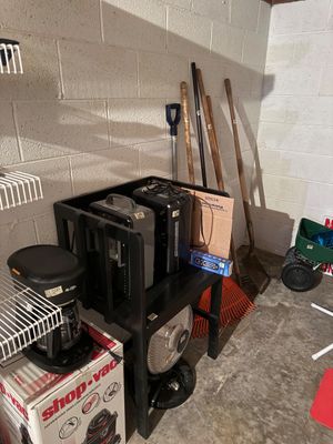 Sale Photo Thumbnail #24: Assorted household and garden items, including a Mr. Coffee coffee maker, space heaters, a floor fan, and various long-handled yard tools like rakes and shovels.