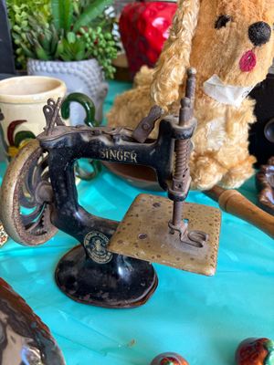 Sale Photo Thumbnail #10: Antique Singer miniature toy sewing machine, showing significant rust and wear consistent with age, displayed alongside a vintage plush dog.