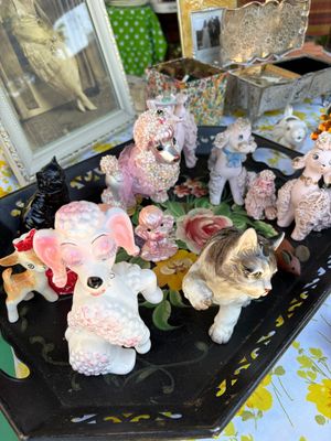 Sale Photo Thumbnail #75: Collection of vintage mid-century ceramic figurines, featuring several pink and white spaghetti poodles, a playful kitten, and a small deer, displayed on a black floral tray.