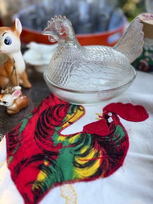 Sale Photo Thumbnail #33: Vintage clear textured glass hen-on-nest covered dish, displayed on a white textile featuring a colorful embroidered rooster applique.