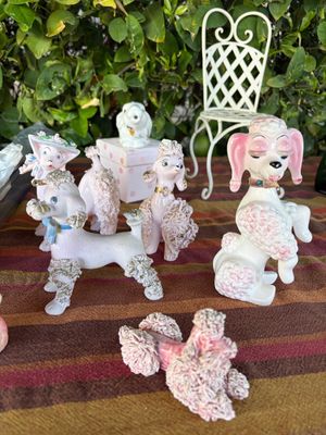 Sale Photo Thumbnail #43: Collection of vintage mid-century ceramic spaghetti poodles and pink dog figurines, displayed alongside a miniature white wire patio chair.