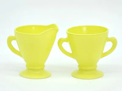 Vintage yellow milk glass creamer and sugar bowl set, featuring a footed pedestal design and classic mid-century styling.