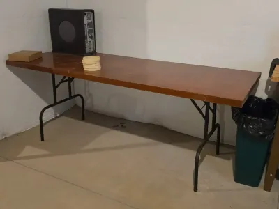 Long rectangular folding table with a brown wood-look laminate top and black metal legs, showing some light surface wear.