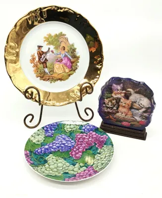 Collection of decorative plates, including a gold-rimmed Fragonard-style courting scene plate on a wire stand, a colorful grape-patterned...