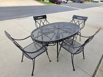 Black wrought iron patio dining set featuring an oval mesh-top table with an umbrella hole and four matching mesh-seat armchairs with ivy...