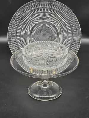 Vintage clear pressed glass serving pieces, including a pedestal cake stand, a shallow bowl with a starburst pattern, and a large platter...
