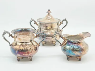 Vintage silver-plated tea service set including a lidded sugar bowl, creamer, and waste bowl, featuring ornate floral embossing and heavy...